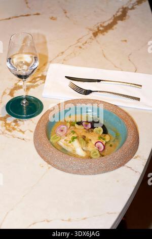 A beautifully plated gourmet dish with vibrant ingredients served alongside a glass of wine, set on a marble table. Ideal for an upscale restaurant di Stock Photo