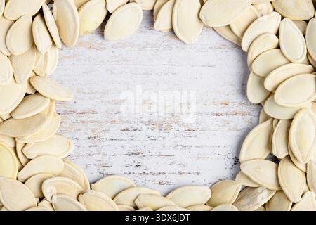 Close-up image of pumpkin seeds placed on a rustic, whitewashed wooden surface, forming a frame around empty space, emphasizing their natural texture Stock Photo