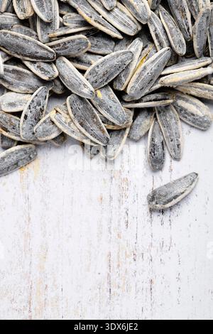 An overhead closeup of salted sunflower seeds scattered over a rustic wooden surface. The seeds' textured shells showcase a contrast of gray and white Stock Photo