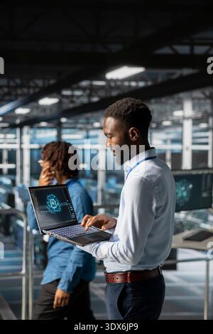 African american technician and coworker in data center reviewing large language model visualizations on PC. Professional IT engineering team analyzing neural network performance outputs. Stock Photo