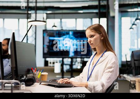 Junior dev in tech startup utilizing AI to optimize performance and forecast issues. Young female engineer writing code in office, training machine learning models using PC Stock Photo