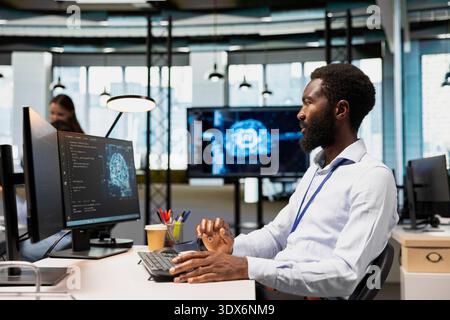 Software developer writing code, developing machine learning APIs. African american man in office working, troubleshooting software errors using artificial intelligence tech Stock Photo