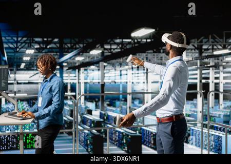 Data center programmer on industrial platform using virtual reality tech, collaborating on tasks. Server room IT professionals visualizing large language model architecture using VR headset. Stock Photo