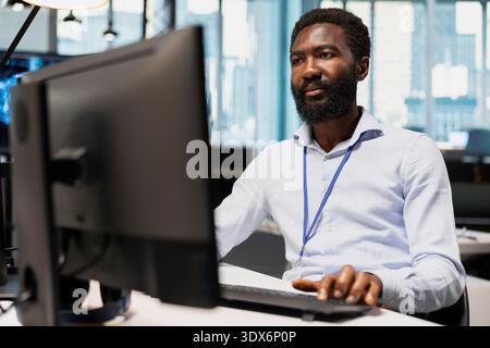 System administrator designing and developing software applications, optimizing code for performance and scalability. African american man in office using PC to resolve bottlenecks Stock Photo