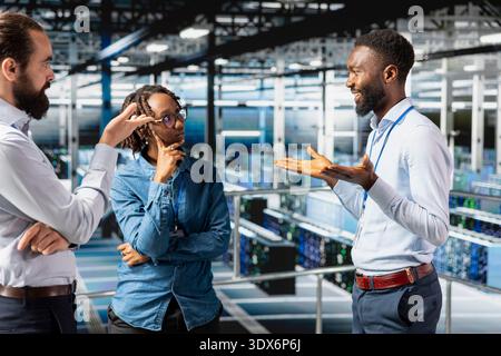 Team of software engineers working on AI automatization in data center, standing on industrial platform. Server farm employees collaborating for server management with artificial intelligence tools. Stock Photo