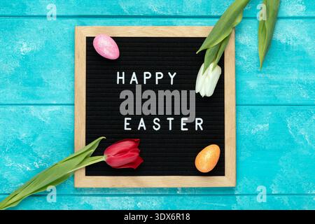 A minimalist and elegant Easter flat lay featuring a black felt letter board with white text reading Happy Easter with glitter Easter eggs and two fre Stock Photo