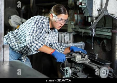 Girl worker at metallurgical plant drills hole in metal plate using drilling machine Stock Photo