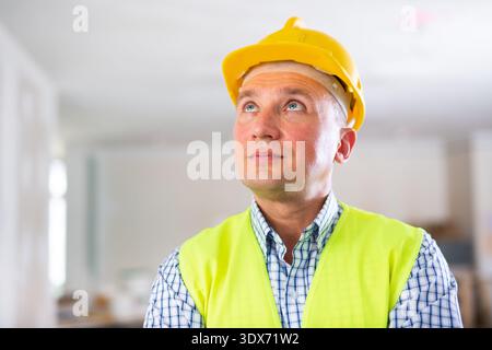 Portrait of smiling worker in yellow vest and hard hat inside cottage under renovation Stock Photo