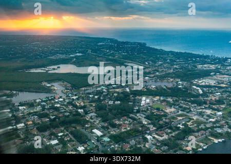 An aerial view shows a coastal town at sunset, with sun rays breaking through the clouds and illuminating the ocean. Stock Photo