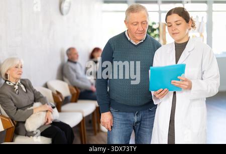 Young nurse or doctor talking with elderly man in reception area Stock Photo