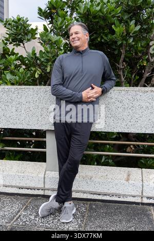 Middle-aged man standing and leaning against speckled planter wall on urban plaza, wearing pullover Stock Photo