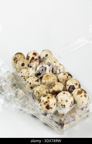 A clear plastic tray holds multiple quail eggs that have speckled shells. The tray appears to be prepared for cooking or selling. Stock Photo