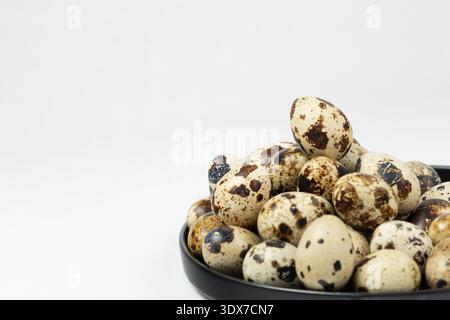 A bowl holds many quail eggs with unique shells marked by brown spots. These eggs are ready for use in various dishes. Stock Photo
