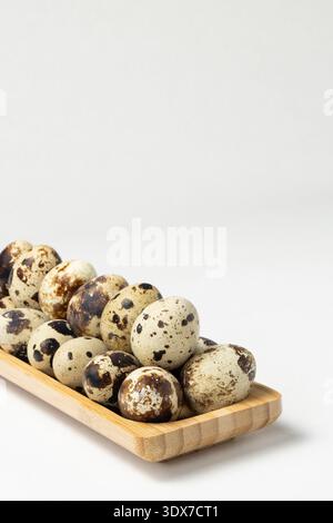 Quail eggs are displayed on a wooden plate. The eggs have dark spots and varying colors. Stock Photo