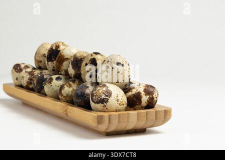 A group of quail eggs sits on a wooden tray. These eggs have dark spots and a light background. The setting is indoors, with a simple and clean look. Stock Photo