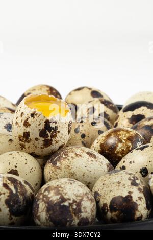 A collection of quail eggs is arranged on a plate. One egg has a broken shell, and the yellow yolk is visible inside. Stock Photo