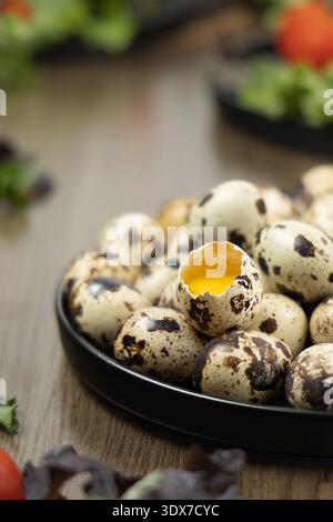 Several quail eggs are placed on a black plate. One of the eggs is cracked open, and the yolk is visible. Stock Photo