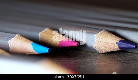 Selective focus on blue, pink, and purple pencil tips lined up on a dark wooden surface Stock Photo