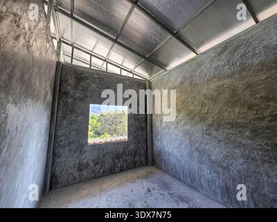 Unfinished interior of an empty room with raw concrete wall and steel roof under construction. hopeful, minimalist architectural design with window lo Stock Photo