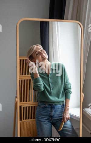 Cheerful smiling woman looking in mirror with positive expression, enjoying appearance in reflection Stock Photo