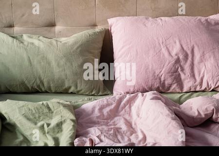 Close up of unmade bed with two pillows. Cozy bedroom bedding with soft wrinkled linen. Interior style and comfort concept. Stock Photo