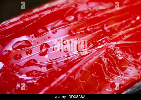 Abstract close up of vibrant red wet surface. Water drop condensation on crinkled plastic background creating an intense and dynamic texture for creat Stock Photo