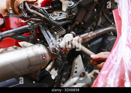 Focused mechanic hand uses hammer tool for motorcycle repair and maintenance. Working with force on metal engine part in workshop, fixing broken bike Stock Photo