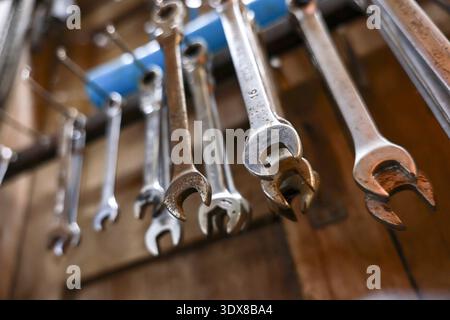 Close up of rustic set of old metal wrench and spanner hanging from rack in workshop. Selective focus on hardworking tool used for repair and maintena Stock Photo