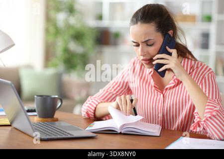 Stressed self employed checking agenda talking on phone working at home Stock Photo