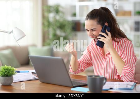 Excited self employed talking on phone receiving good news working at home Stock Photo