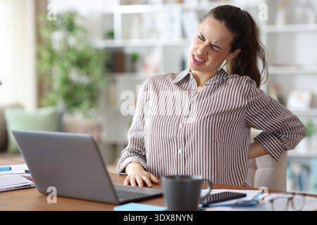 Teleworker suffering back ache while is working online at home Stock Photo