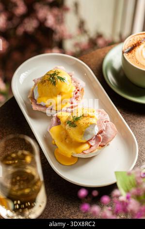 A top-down view of two perfectly poached eggs served on English muffins with sliced ham, generously topped with smooth yellow hollandaise sauce and fr Stock Photo