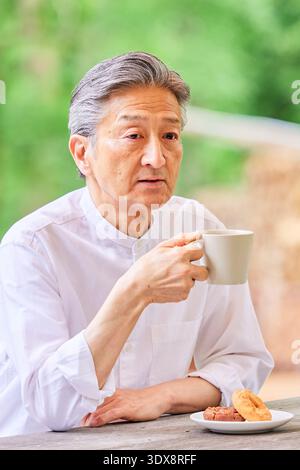 Senior Asian man drinking coffee on a terrace Stock Photo