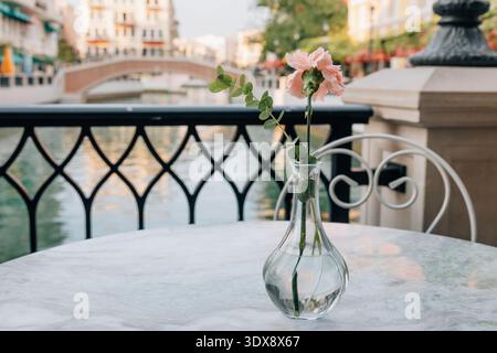 Carnation in a glass vase on a marble table at an outdoor cafe or restaurant with a canal and bridge in the background Stock Photo