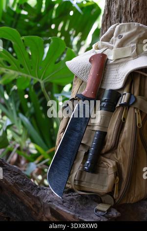 machete knife and a hiking backpack rest on a log. Stock Photo