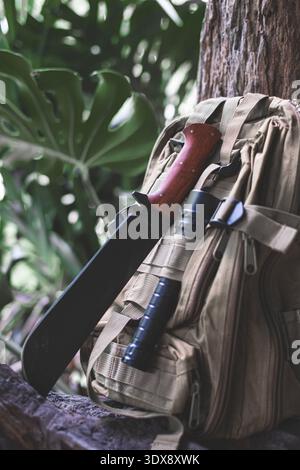 A machete knife and a hiking backpack rest on a log. Stock Photo