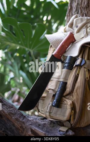 A machete knife and a hiking backpack rest on a log. Stock Photo