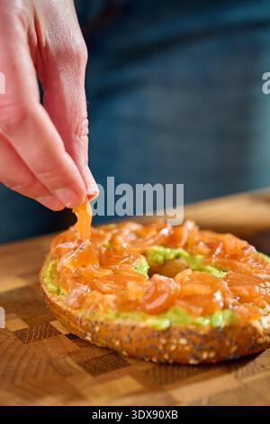 Avocado bagel with smoked salmon on cutting board during breakfast preparation Stock Photo