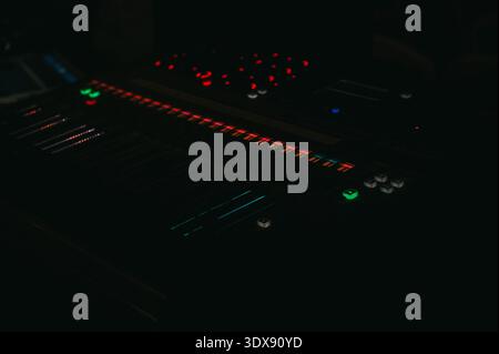 Riga, Latvia - February 24, 2023:Close-up of a professional audio mixing console illuminated in a dark studio environment. Dramatic low-light scene wi Stock Photo