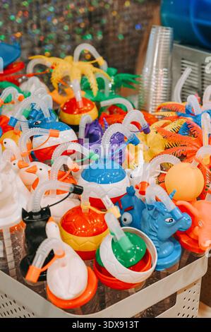 Riga, Latvia - February 28, 2026:Close up of bright plastic novelty drink cups shaped as animals, balls and tropical elements with flexible straws. Vi Stock Photo