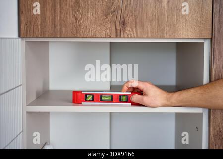 Close up of hands placing spirit level on cabinet shelf inside kitchen cabinet. Using bubble level to verify level during furniture assembly Stock Photo