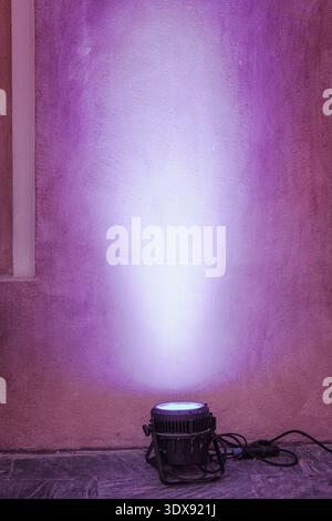 Purple stage spotlight casts a vertical luminous beam across a textured stone wall, creating moody glow and theatrical atmosphere Stock Photo