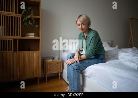 Unmotivated tired woman sitting on bed showing signs of apathy and burn out, personal life crisis. Stock Photo
