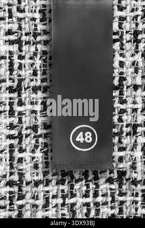 Size 48 clothes label over white and black tweed fabric background Stock Photo