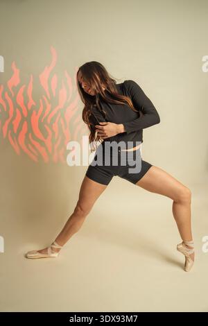 Female dancer performing a dynamic move, showing emotion and strength with projected flame pattern Stock Photo