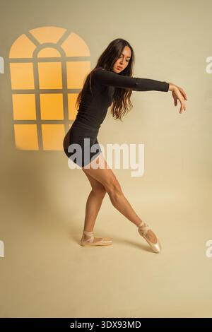 Ballerina balancing gracefully in pointe shoes, illuminated by window shaped light Stock Photo