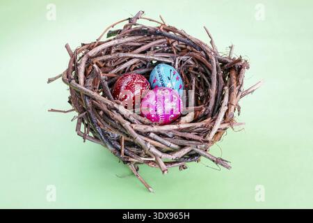 Three hand painted easter eggs in bird's nest over light green background Stock Photo