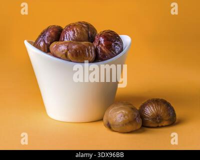 Bunch of Spanish chestnuts in white ceramic bowl on orange background Stock Photo