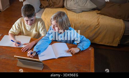Two boys are studying and doing schoolwork at home, using a tablet and notebooks Stock Photo