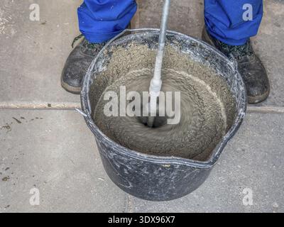 Construction worker mixing mortar in a bucket using handheld concrete mixer Stock Photo